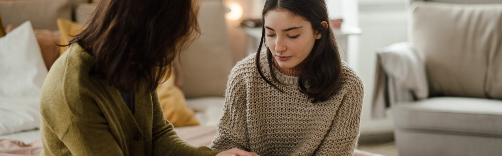 A mother and daughter sitting on a bed while having a conversation