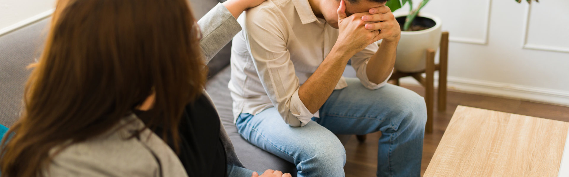 A man sitting on a couch while covering his face while and listening some advice to a psychiatrist